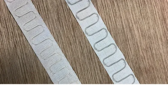 Two lengths of white woven tape on a wooden surface, each carrying a looping serpentine antenna path along its length