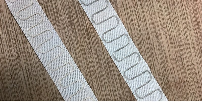 Two lengths of white woven tape on a wooden surface, each carrying a looping serpentine antenna path along its length