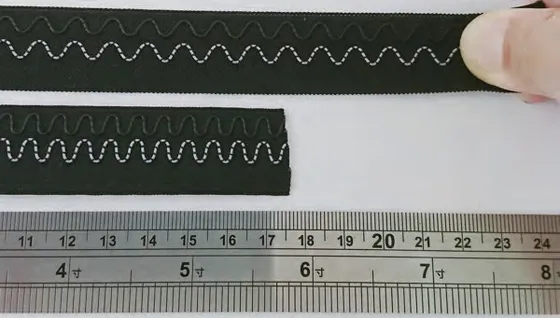 Two lengths of dark woven tape carrying a pale conductive wire in a repeating wave, held against a steel ruler marked in centimetres
