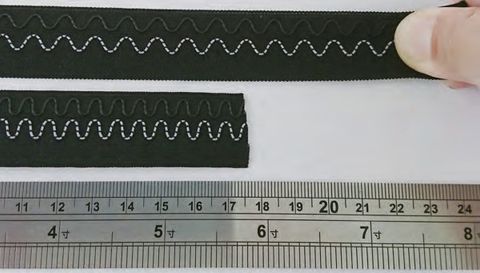 Two lengths of dark woven tape carrying a pale conductive wire in a repeating wave, held against a steel ruler marked in centimetres